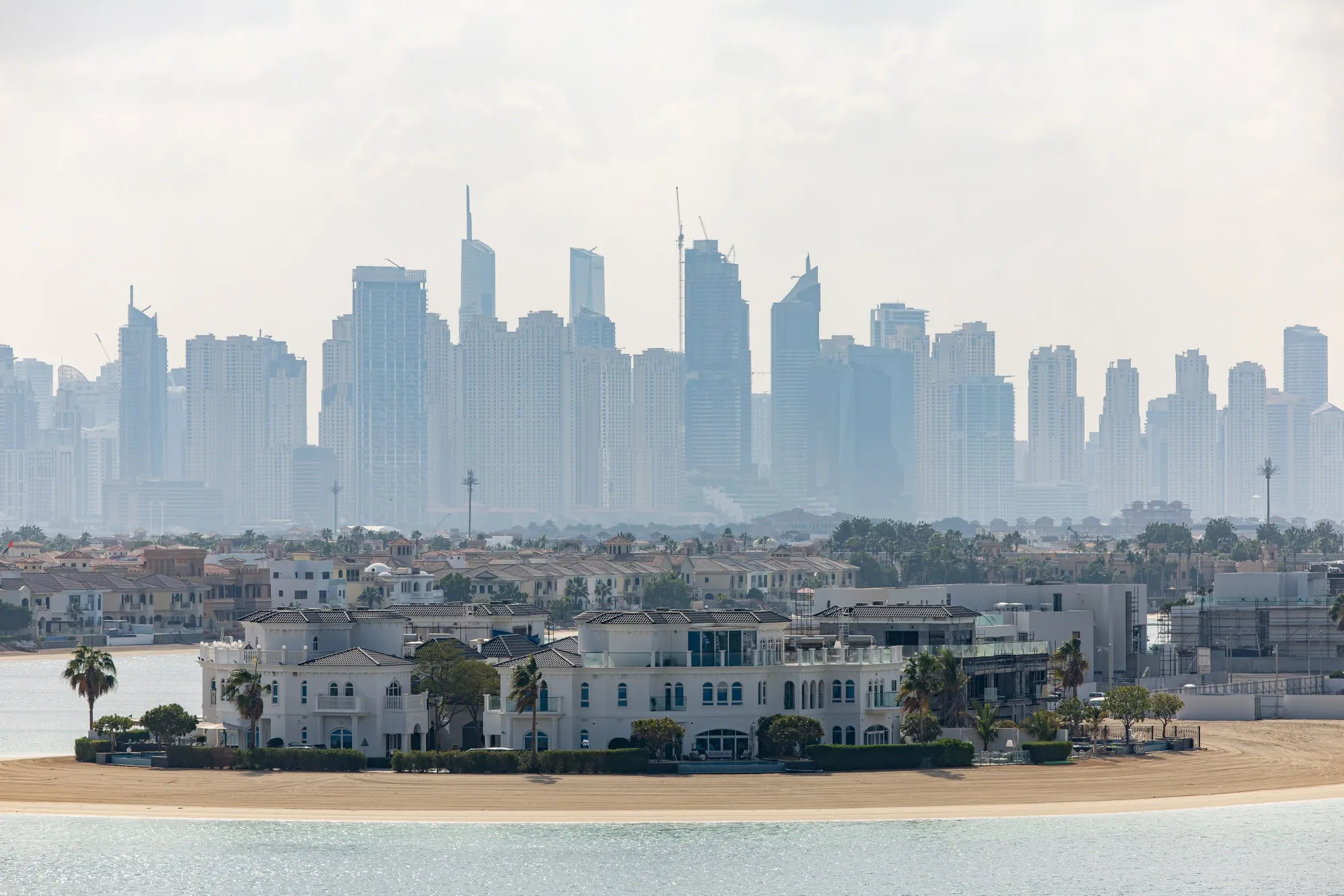 Residential skyscraper buildings beyond luxury villas on the waterfront of the Palm Jumeirah in Dubai.