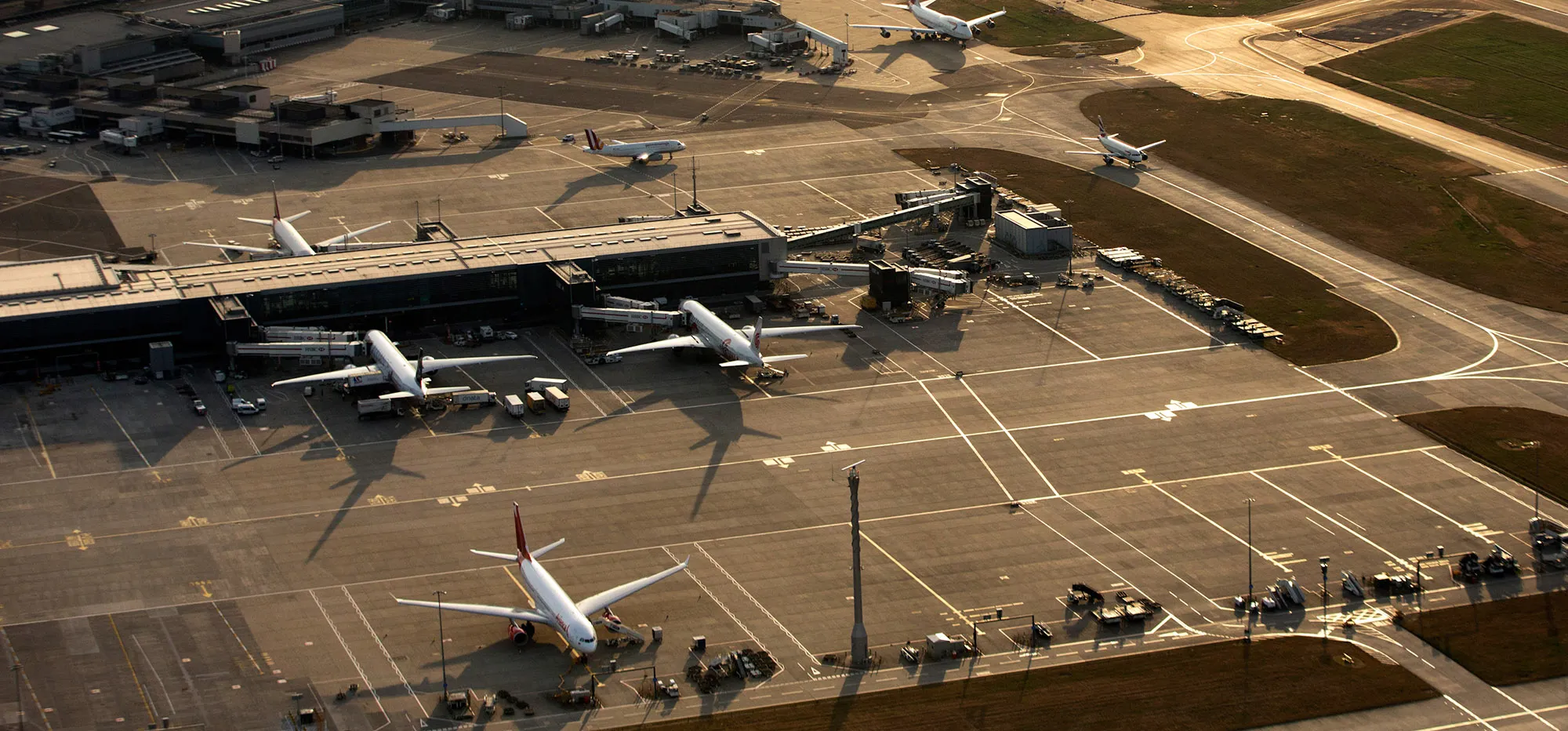 Aircrafts taxi along the perimeter of the north runway, center, and past passenger terminal buildings at London Heathrow Airport.