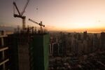 Cranes stand at a construction site as as buildings stand in the background at dusk in the Makati district of Manila, the Philippines.