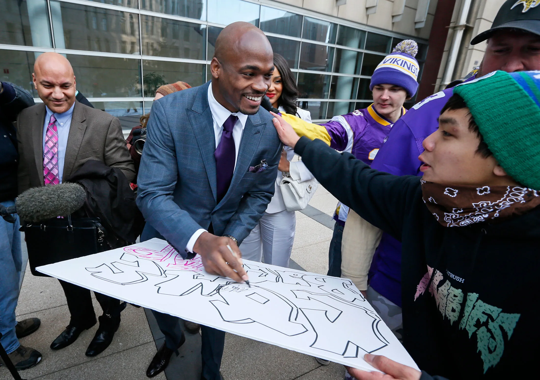 Adrian Peterson signs a poster for Brady Vixayvong of Eagen as he and his wife Ashley leave the federal court house on Feb. 6, 2015 in Minneapolis.
