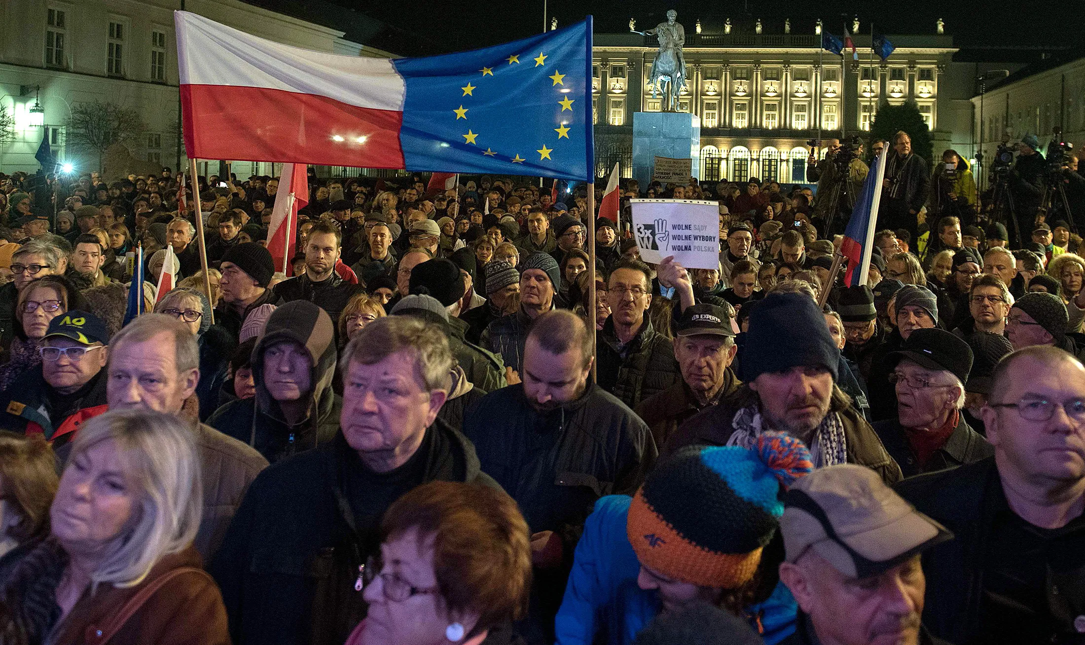 People hold up a Polish and EU flag and copies of the Constitution as they gather in front of the presidential palace in Warsaw under the slogan "Free courts, free elections, free Poland."