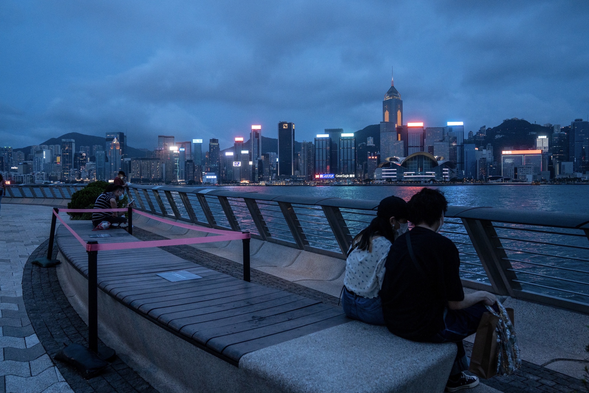 Visitors sit on a bench along the promenade at Victoria Harbour in the Tsim Sha Tsui district of Hong Kong.