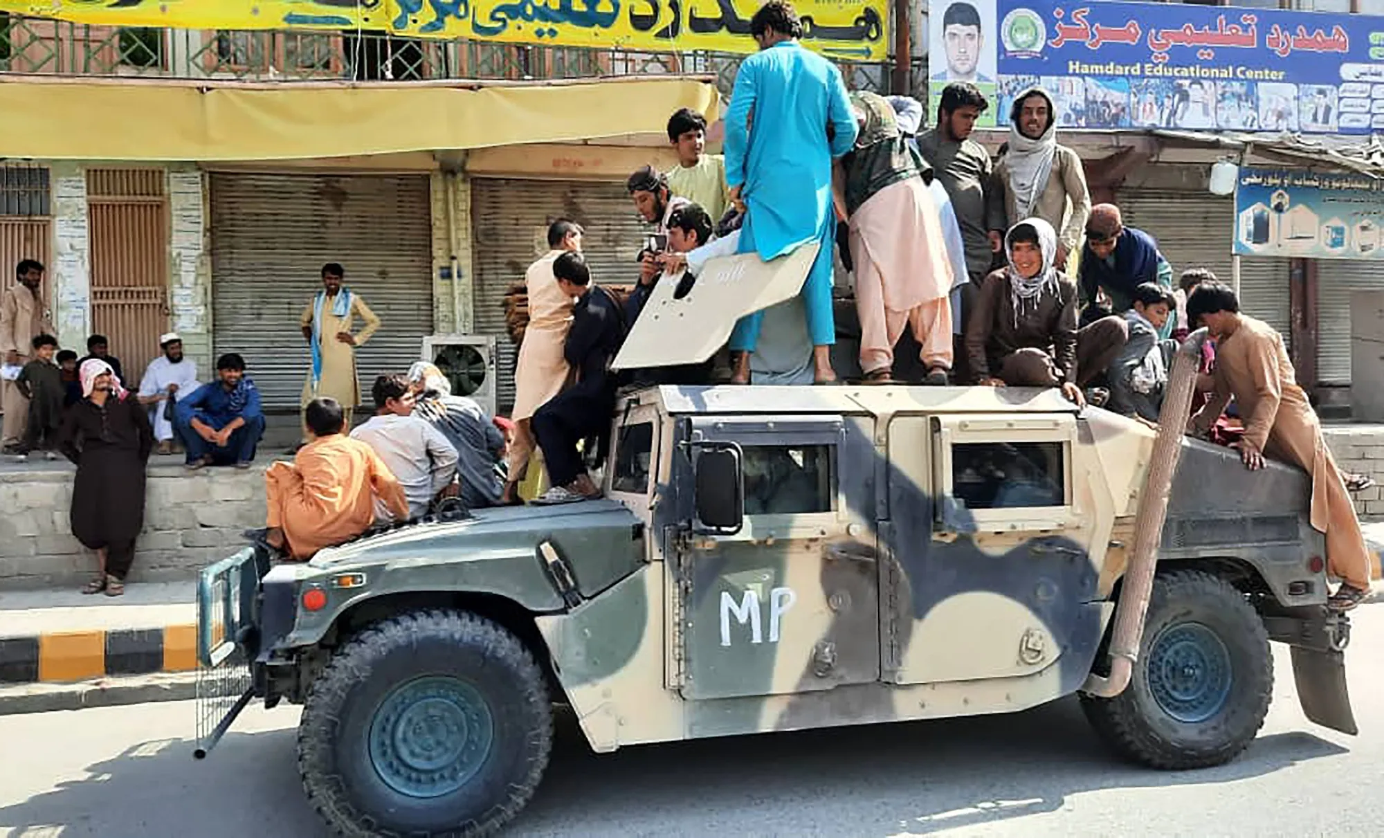 Taliban fighters and local residents sit on an Afghan National Army vehicle in Laghman province on Aug. 15.