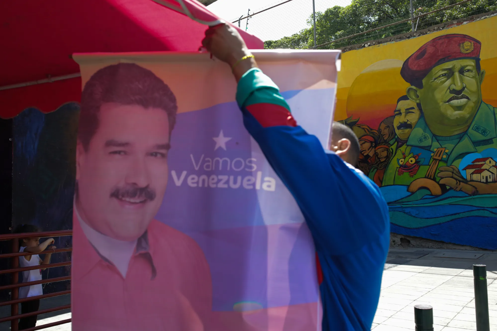 A pro-government supporter hangs a campaign poster for Nicolas Maduro