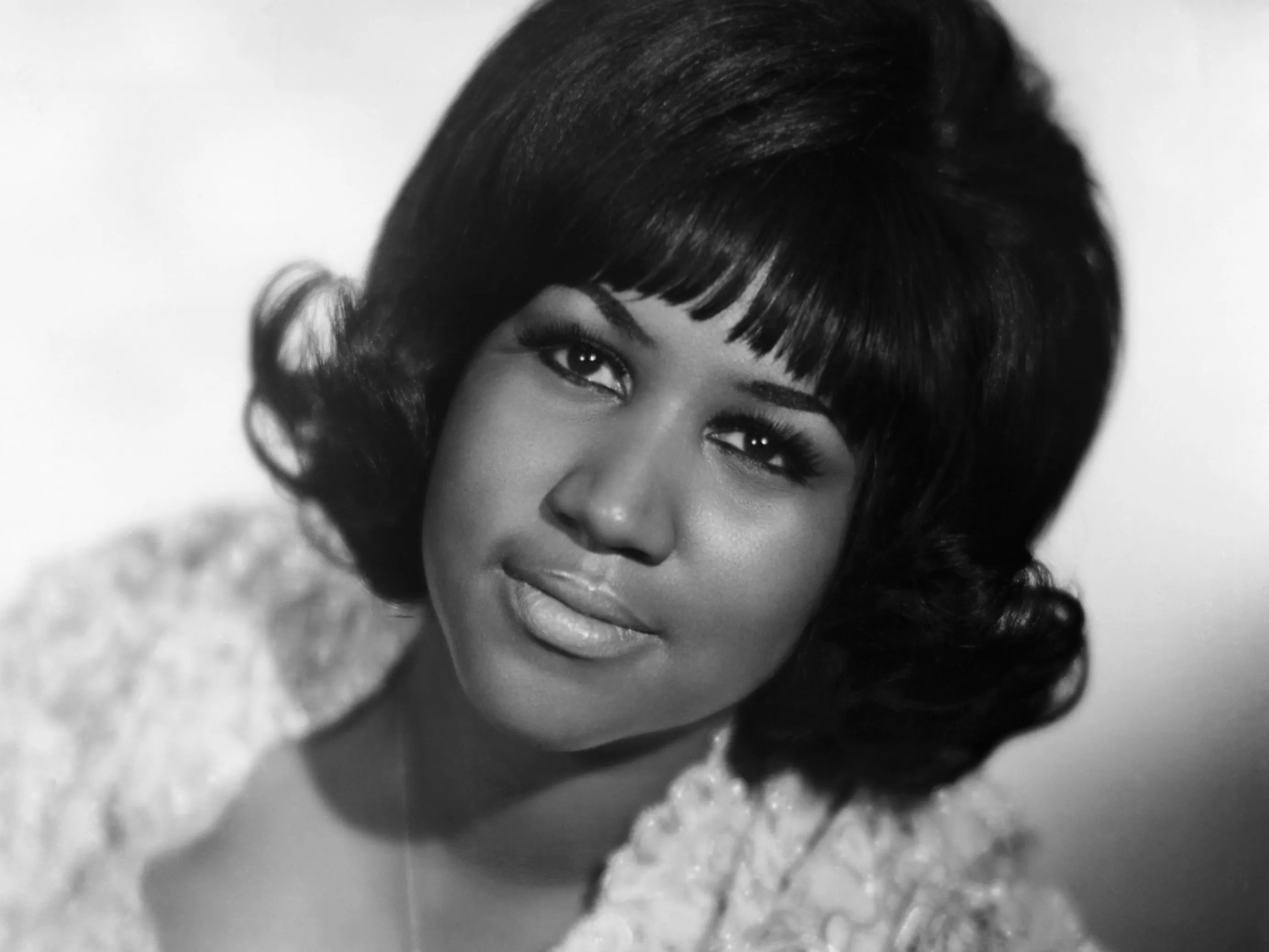 Seated portrait of R&B singer Aretha Franklin during her youth. In this photo her left hand is featured prominently with a diamond bracelet on her wrist and engagement ring on her finger.
