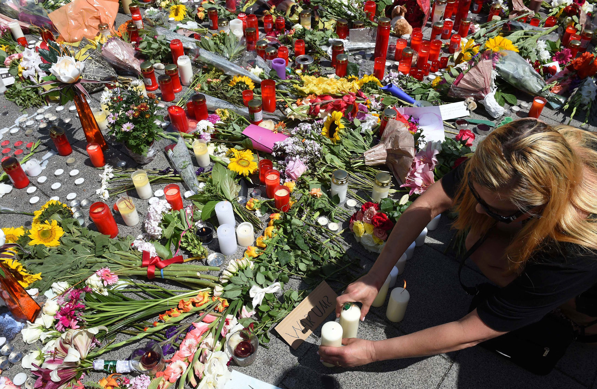 A woman places a candle at a memorial in front of the Olympia Einkaufszentrum shopping center in Munich, on July 24, 2016.

