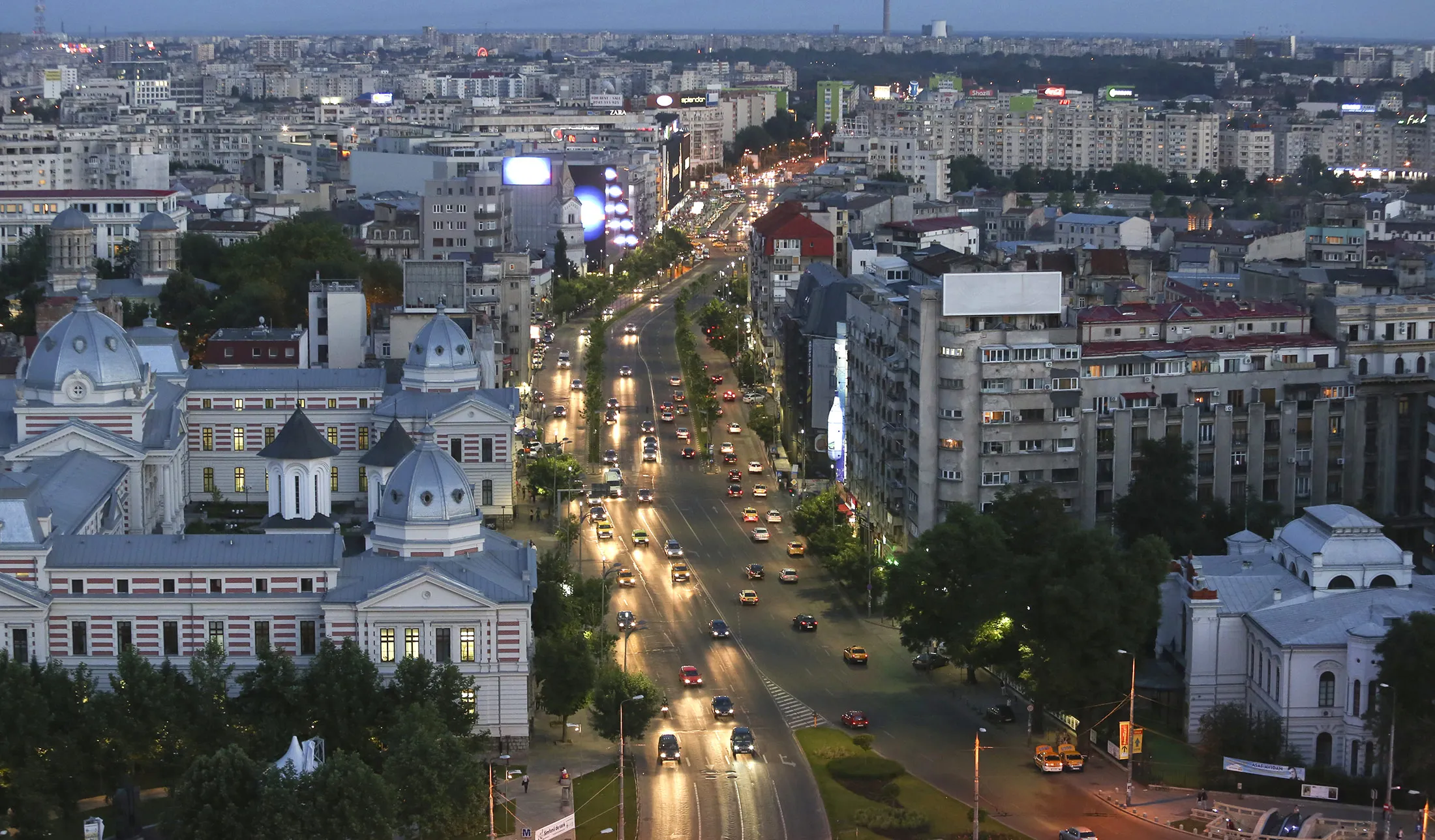 Automobile headlights illuminate a road in the late evening light, as traffic moves towards the University roundabout in the center of Bucharest, Romania.