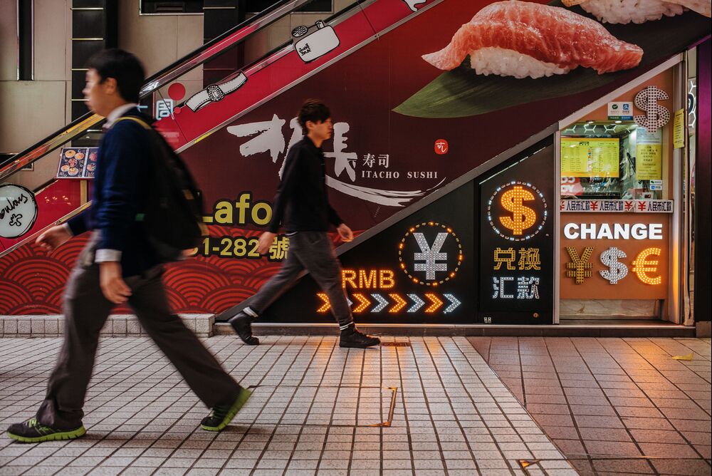 Pedestrians walk past a currency exchange store located under an escalator in Hong Kong, China, on Thursday, March 16, 2017.