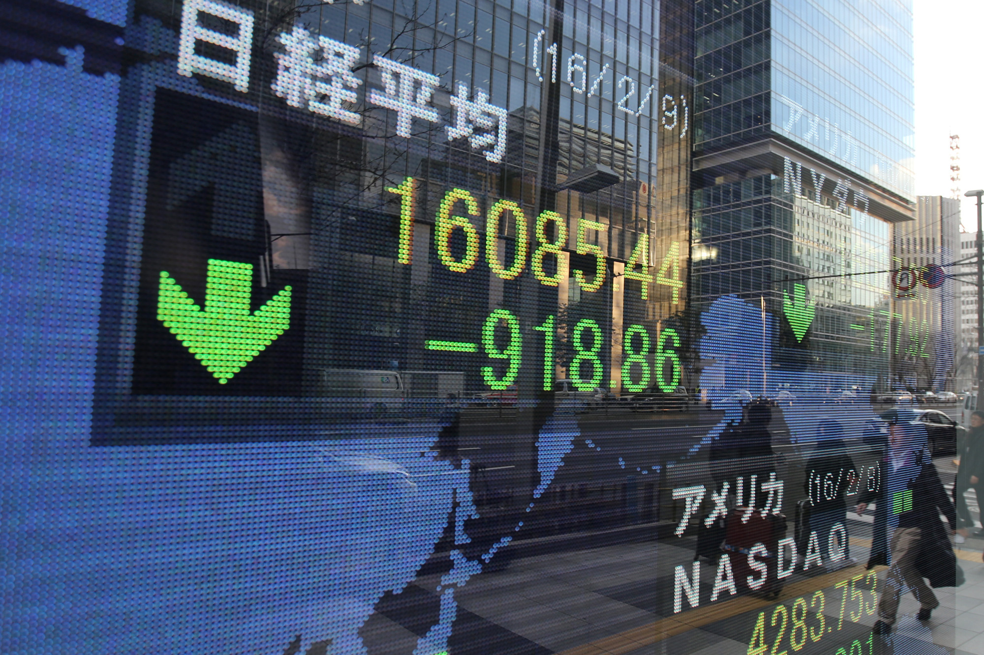 Pedestrians are reflected in an electronic board displaying the closing price of the Nikkei 225 Stock Average outside a securities firm in Tokyo, Japan, on Tuesday, Feb. 9, 2016.
