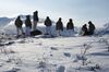 Eight soldiers stand on a snowy, rocky ridge looking toward the Alaska Range in the distance, which is wrapped in slivers of mist.