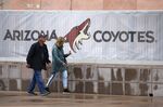 A couple walks past the Gila River Arena, home of the Arizona Coyotes NHL hockey club, March 12, 2020, in Glendale, Ariz. The Coyotes are all caught up on their bills. No eviction necessary. The hockey team in the desert paid off its overdue bills on Thursday, Dec. 9, 2021, a day after receiving word that the City of Glendale was going to lock them out of their arena if they didn't get caught up. Glendale city manager Kevin Phelps sent a letter on Wednesday informing the Coyotes they owe $1.3 million, including $250,000 to the city. (AP Photo/Ross D. Franklin, file)