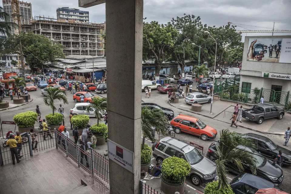 Pedestrians pass heavy road traffic outside an Orabank bank branch, right, in the financial district of Abidjan, Ivory Coast.