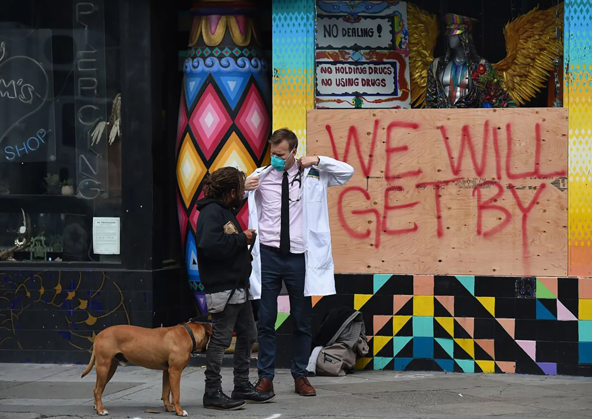 A doctor speaks with homeless people about the coronavirus in front of a boarded-up shop in the Haight Ashbury area of San Francisco California.