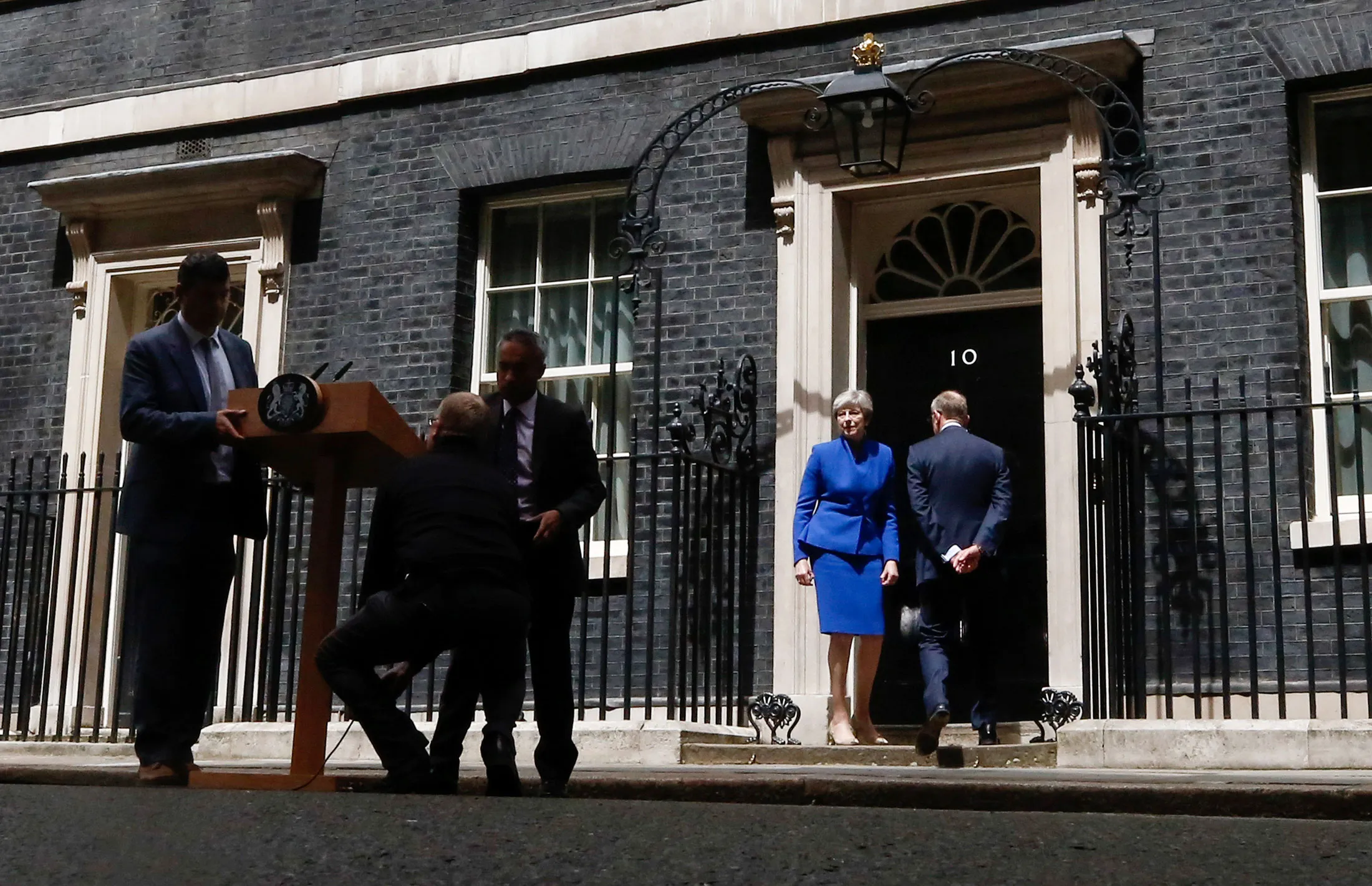 Theresa May, U.K. prime minister and leader of the Conservative Party, center, and her husband Philip May, walk back into number 10 Downing Street, as workers disassemble a podium following her speech, in London, U.K., on Friday, June 9, 2017. May's future as Britain's prime minister was thrown into doubt after her gamble to call an early election backfired spectacularly just 10 days before Brexit negotiations are due to start.
