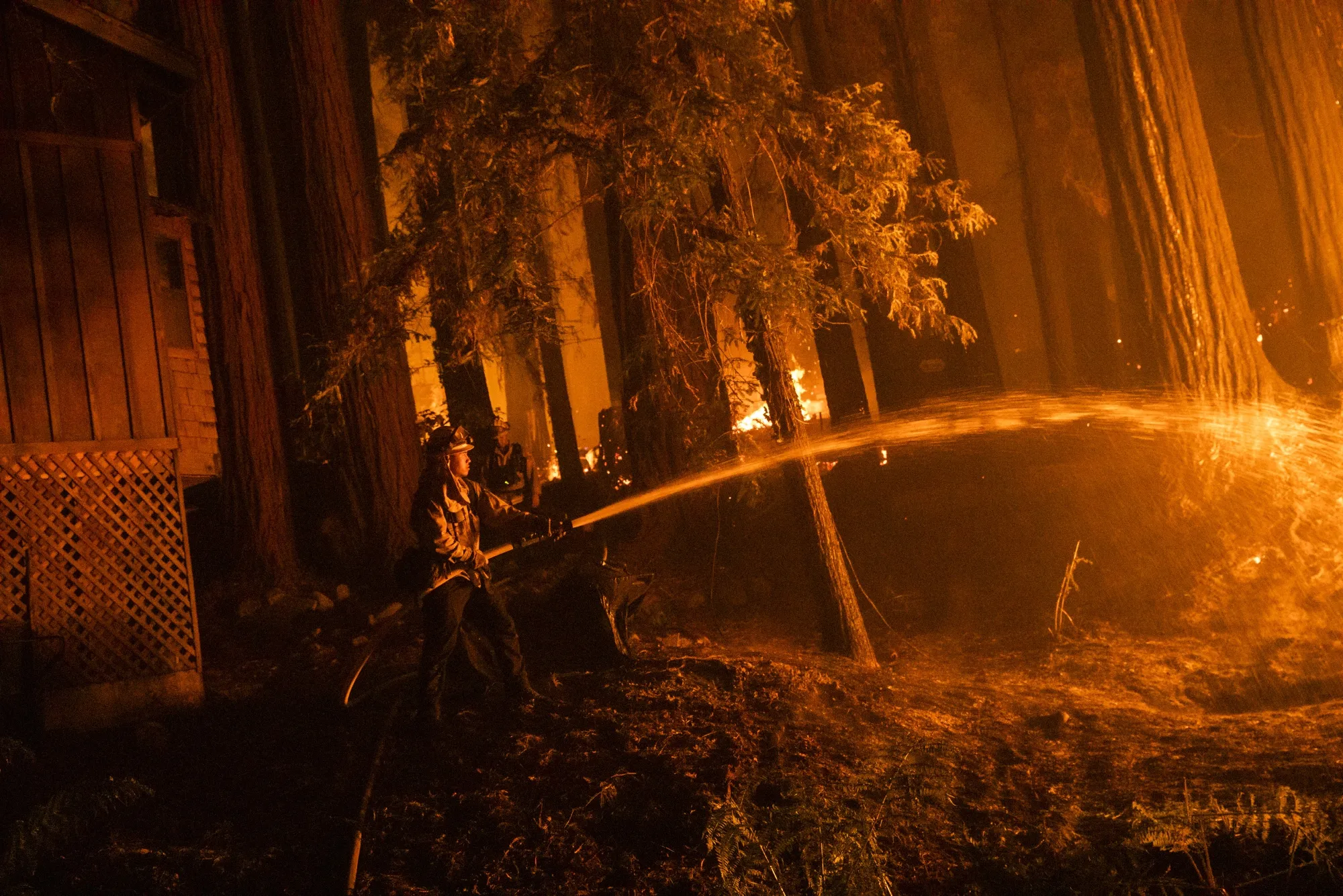 A firefighter protects a home as flames approach during the CZU Lightning Complex fire in Santa Cruz County, California in Aug. 2020.