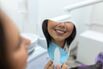 Smiling woman checks her teeth in a handheld dental mirror at a bright clinic