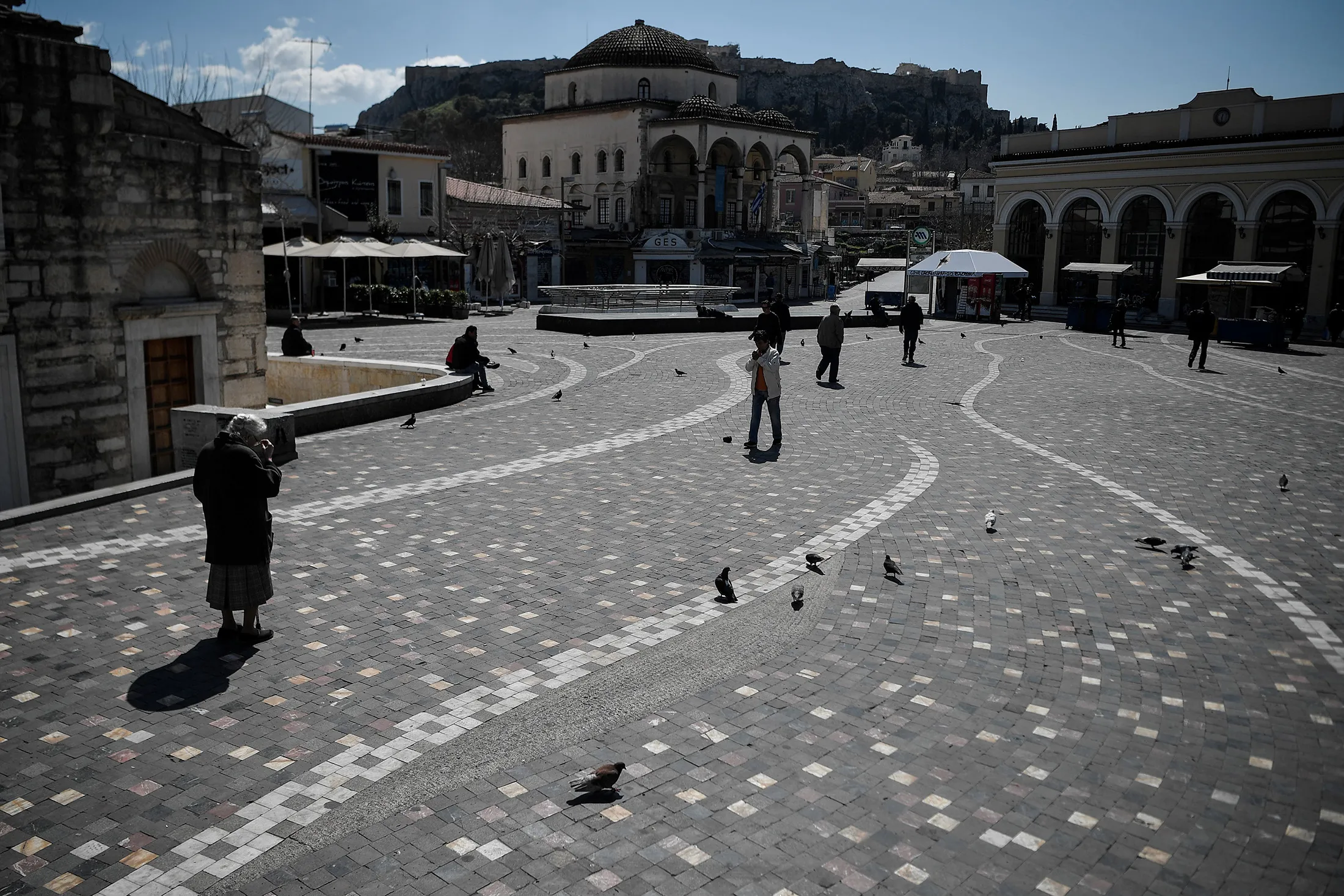 People walk across the empty Monastiraki square under the Acropolis in central Athens, on March 18.