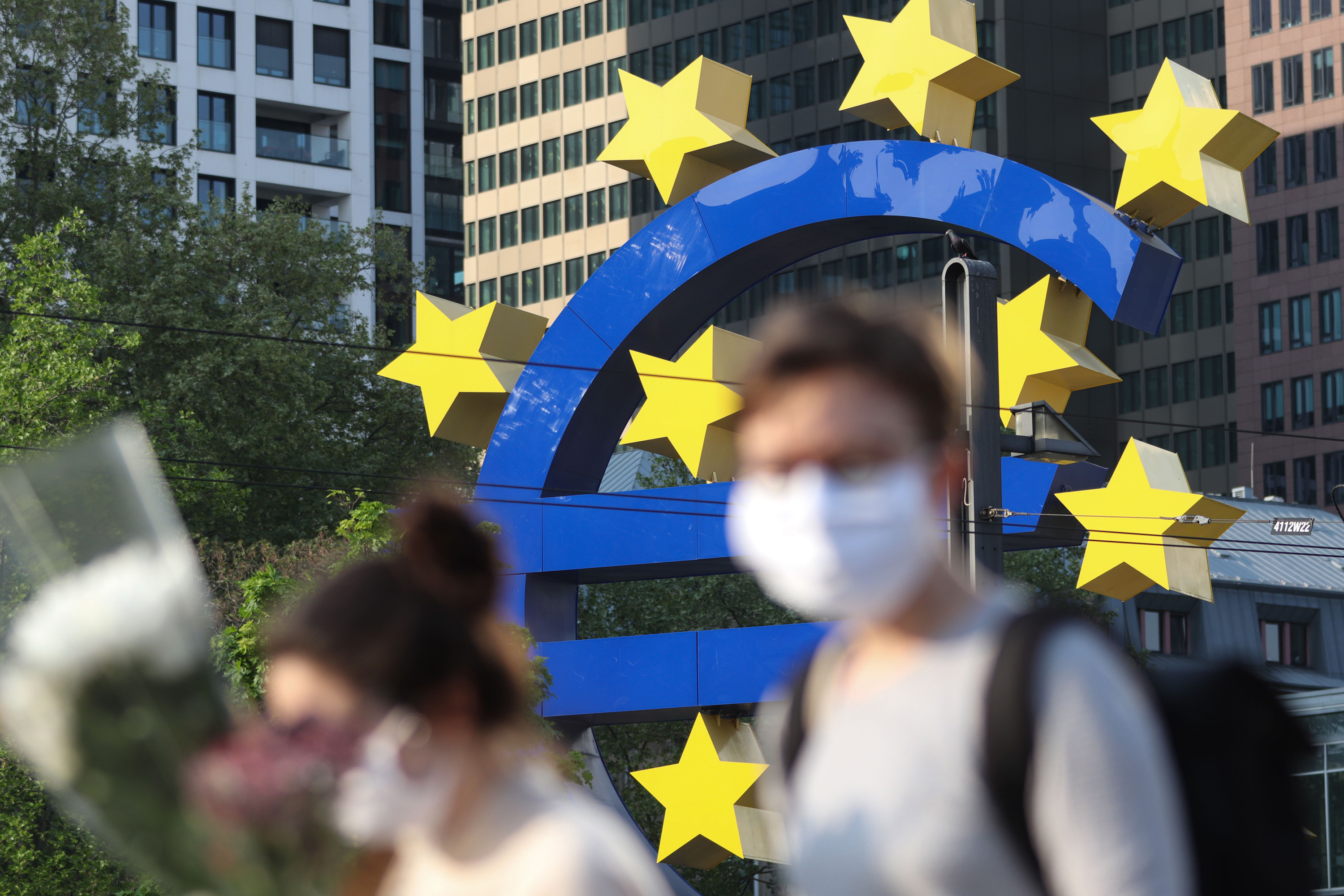 People wearing face masks pass a Euro sculpture in Frankfurt.