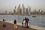 Visitors pose for photographs on the waterside on Palm Jumeirah island with a view of Dubai Marina district in Dubai.