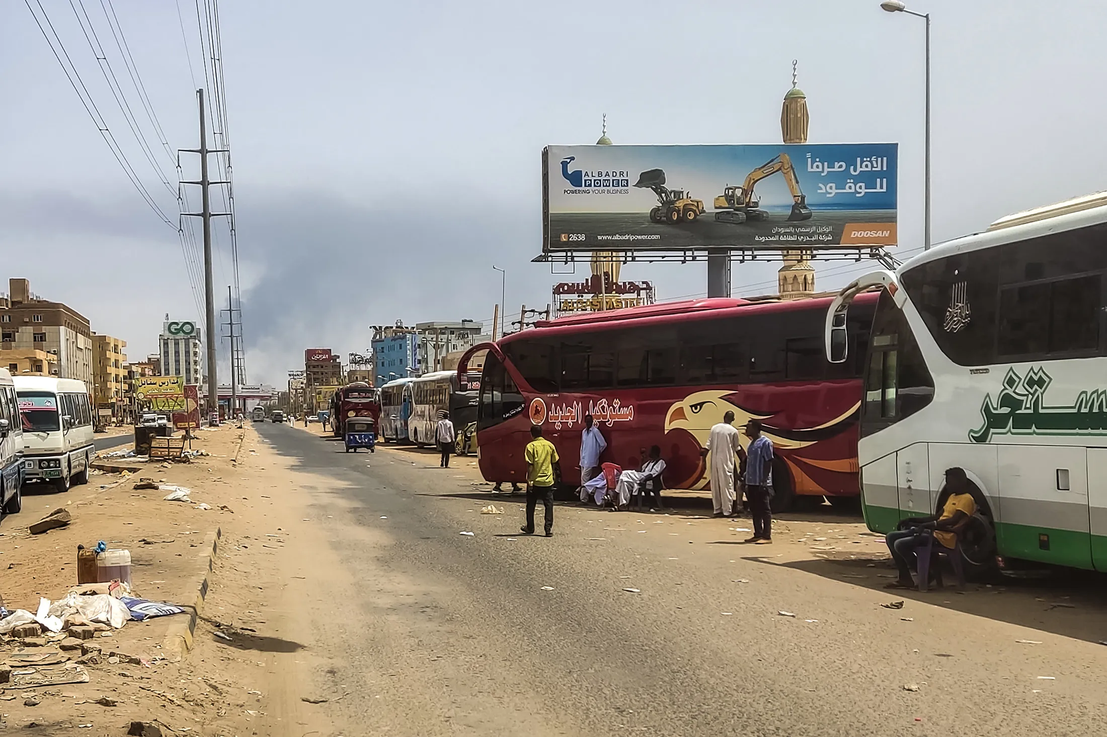 People wait next to passenger buses as smoke billows in an area in Khartoum where fighting continues between Sudan's army and the paramilitary forces on April 28.