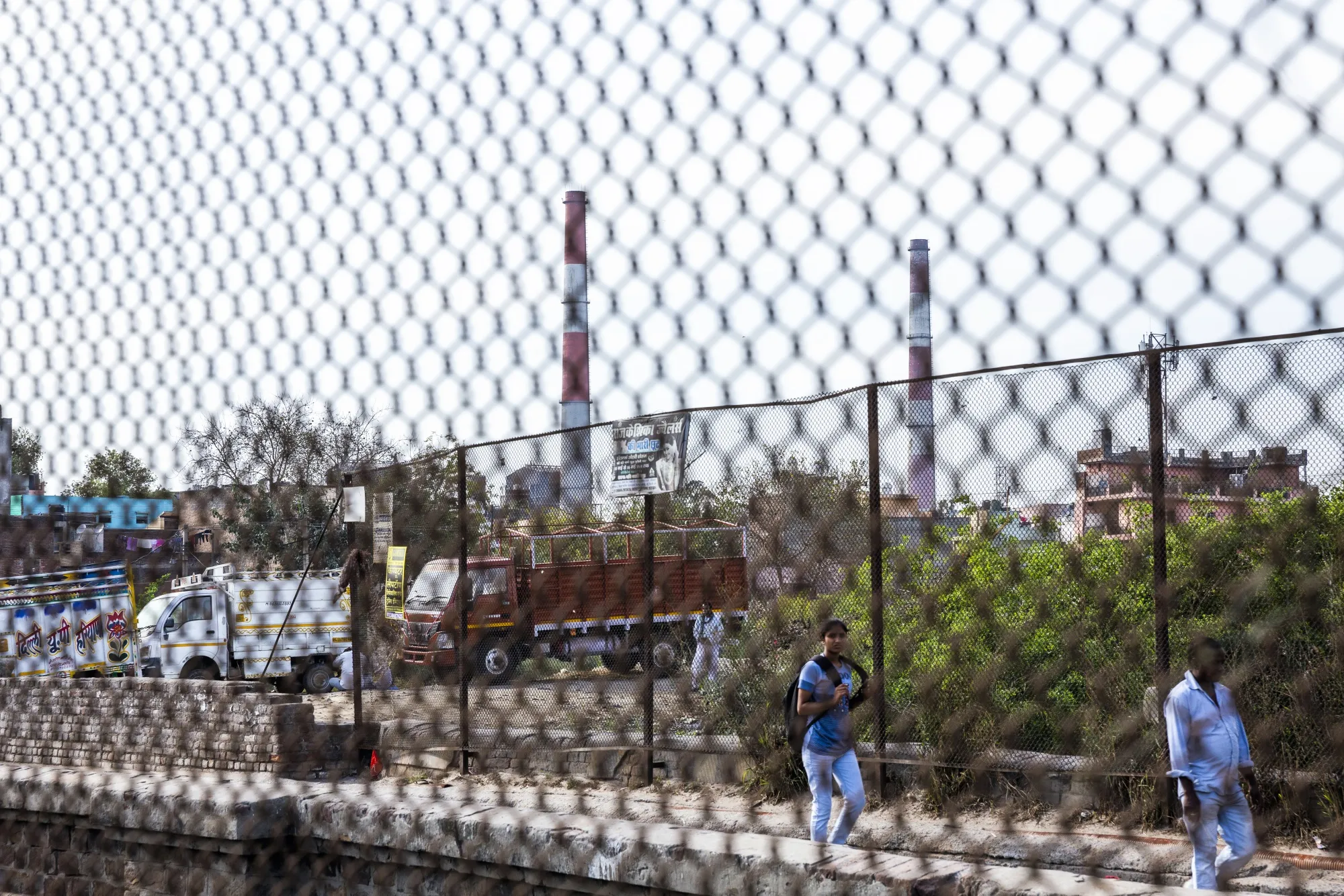 Pedestrians walk along a street as smokestacks of the closed coal-fired NTPC Ltd. Badarpur Thermal Power Station stand in the background in Badarpur, Delhi, India, on Wednesday, March 27, 2019.