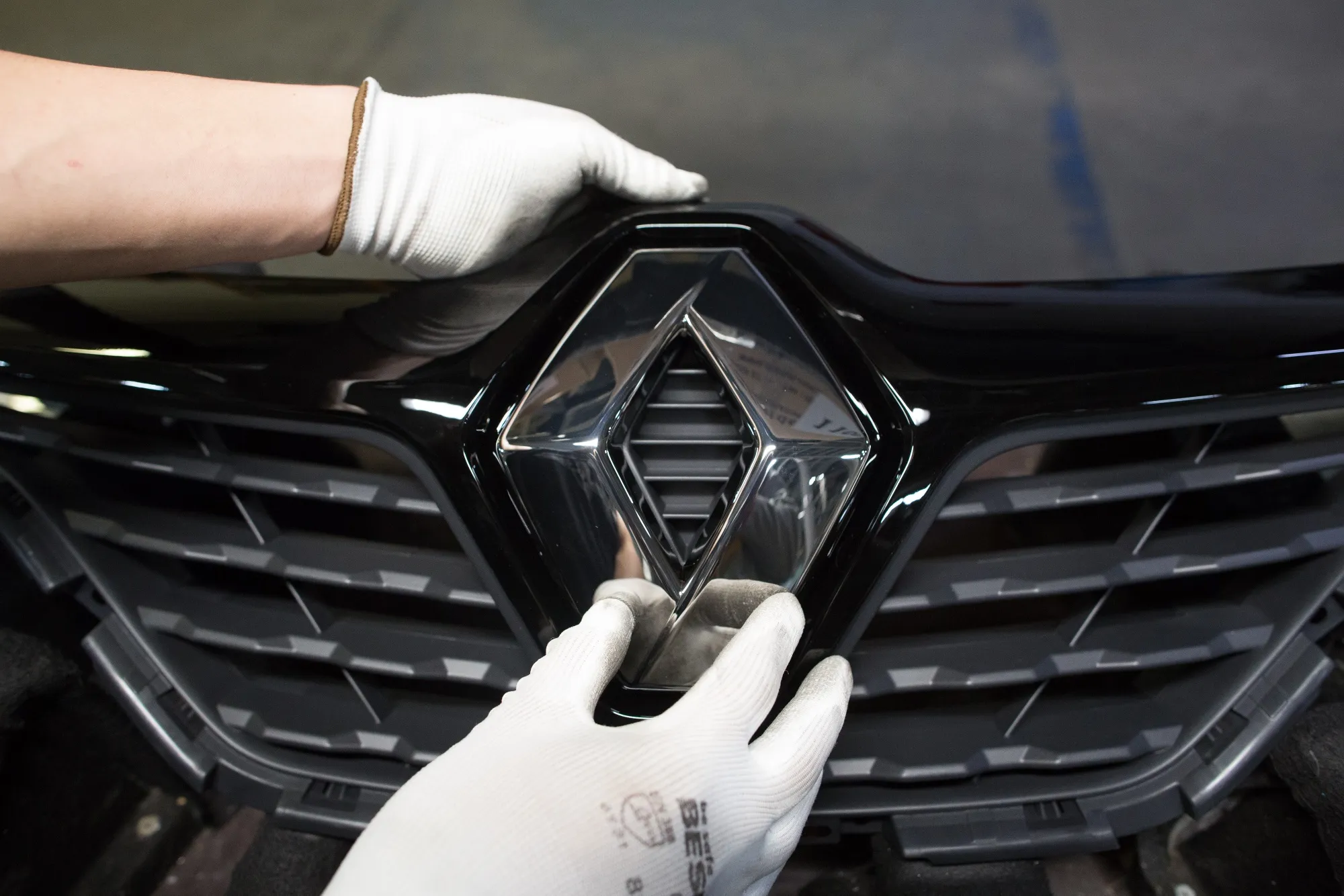 A worker attaches a Renault diamond badge to the front grille of an automobile on the production line inside the Renault SA automobile plant in Moscow, Russia.