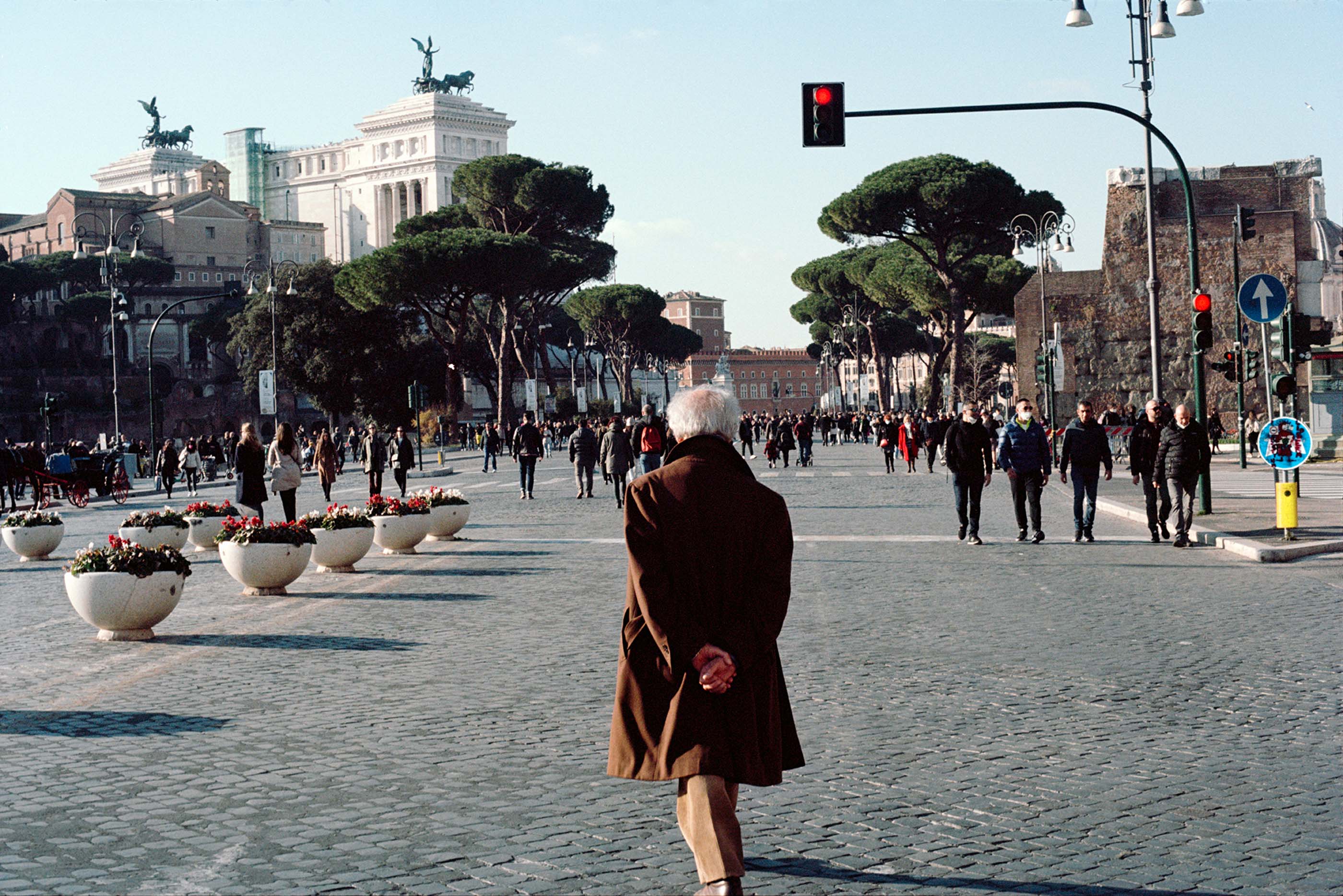 An older gentleman in a dapper coat walks towards the Via dei Fori Imperiali in Rome.