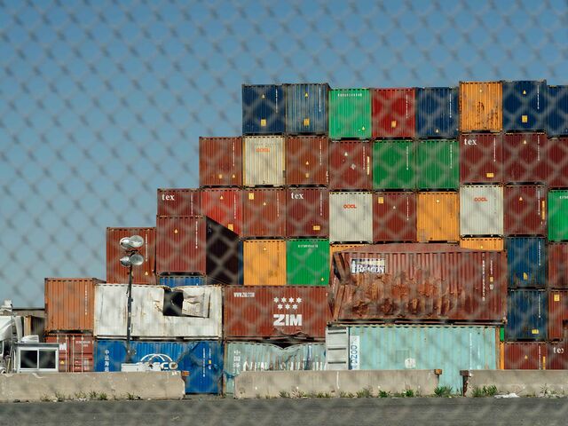 Photo showing a variety of stacked shipping containers outdoors at a port.