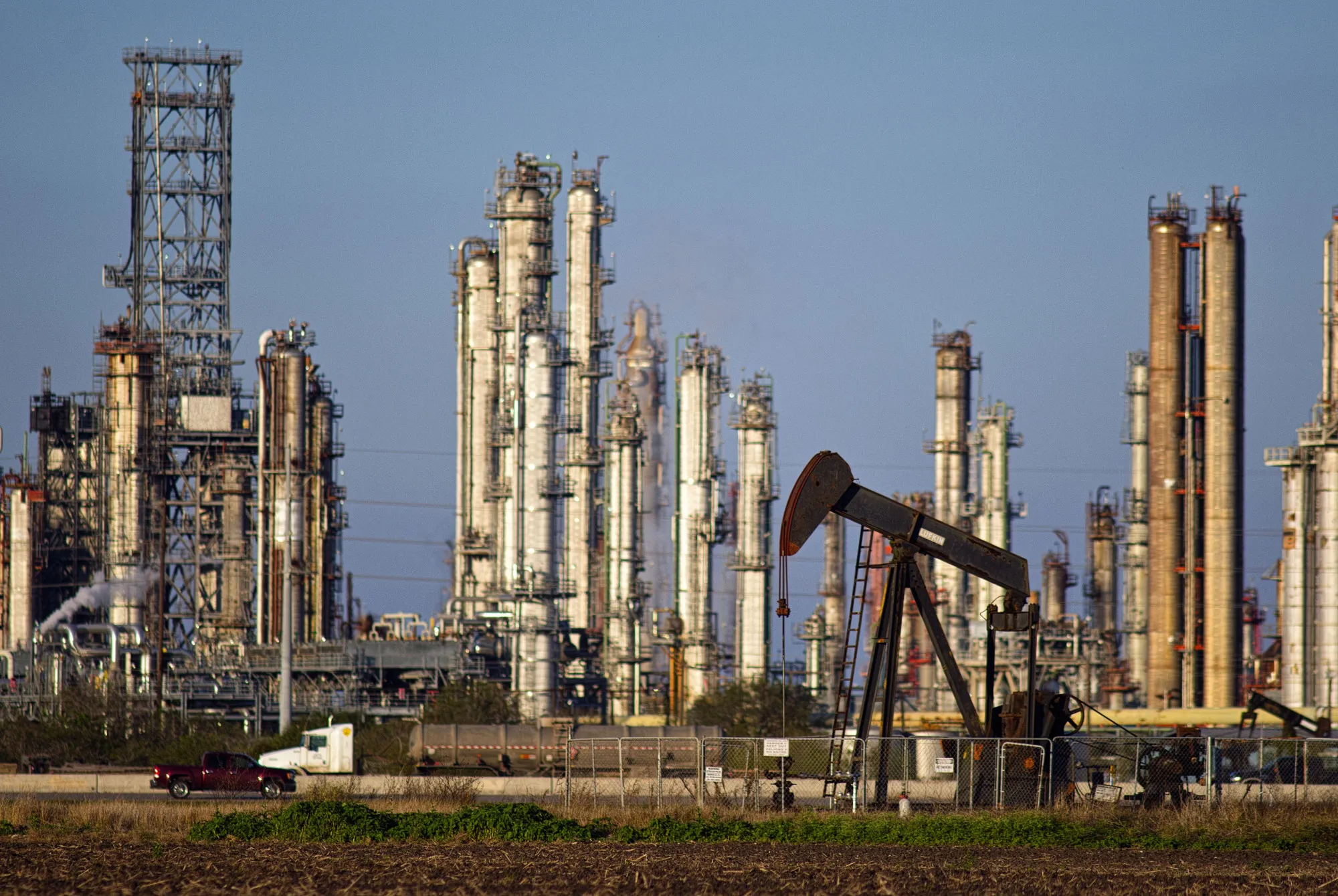 A refinery stands in the background as a pump jack operates in an oil field near Corpus Christi, Texas, U.S., on Thursday, Jan. 7, 2016.&nbsp;