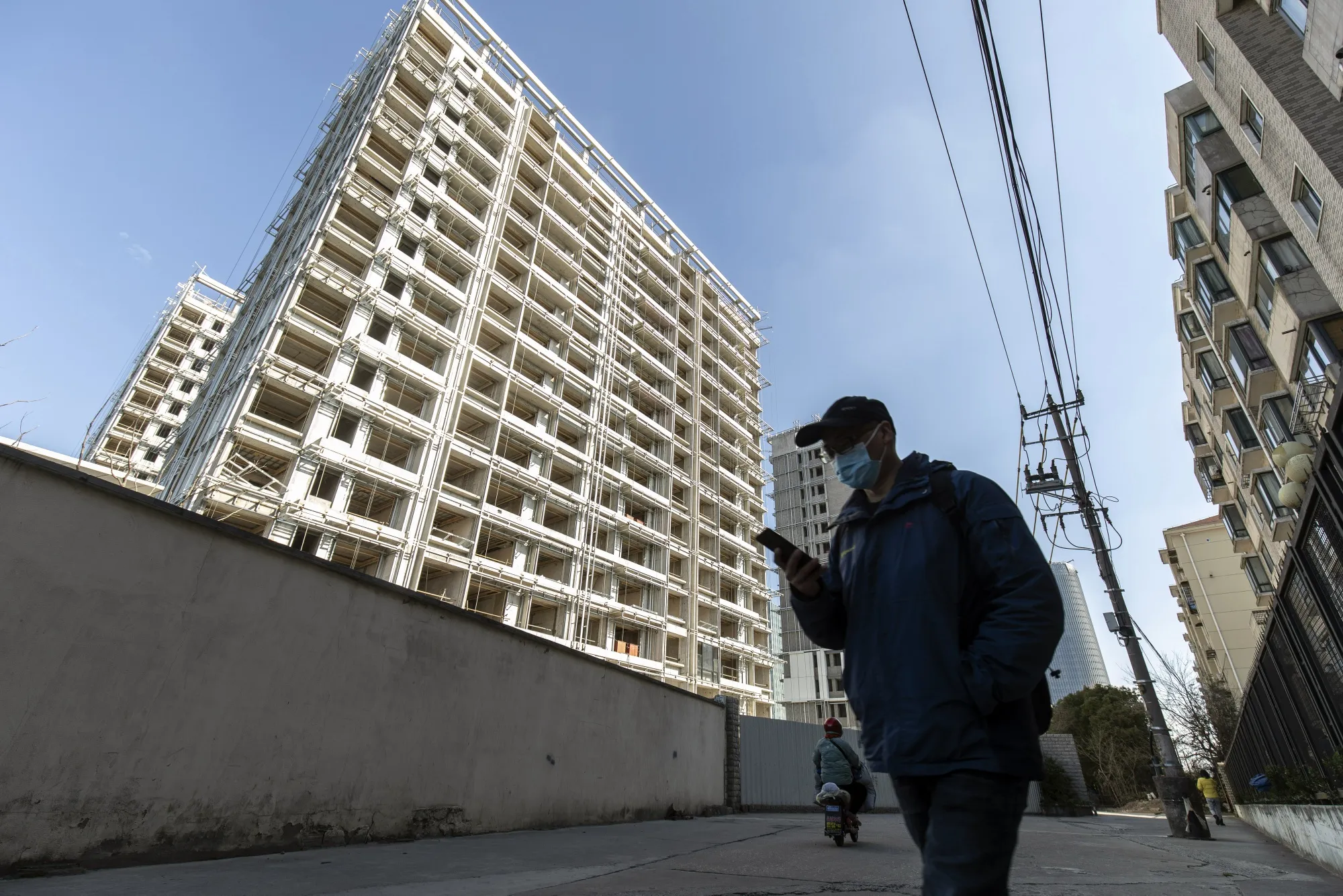 A pedestrian passes unfinished apartment buildings at construction site developed by Sunac China Holdings Ltd., in Shanghai.
