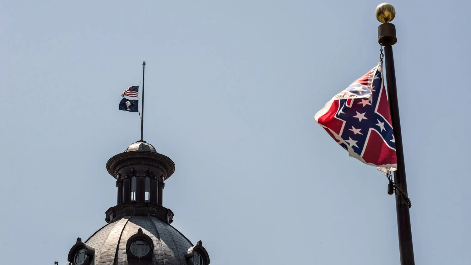 The South Carolina and American flags fly at half mast as the Confederate flag unfurls below at the Confederate Monument June 18, 2015 in Columbia, S.C.
