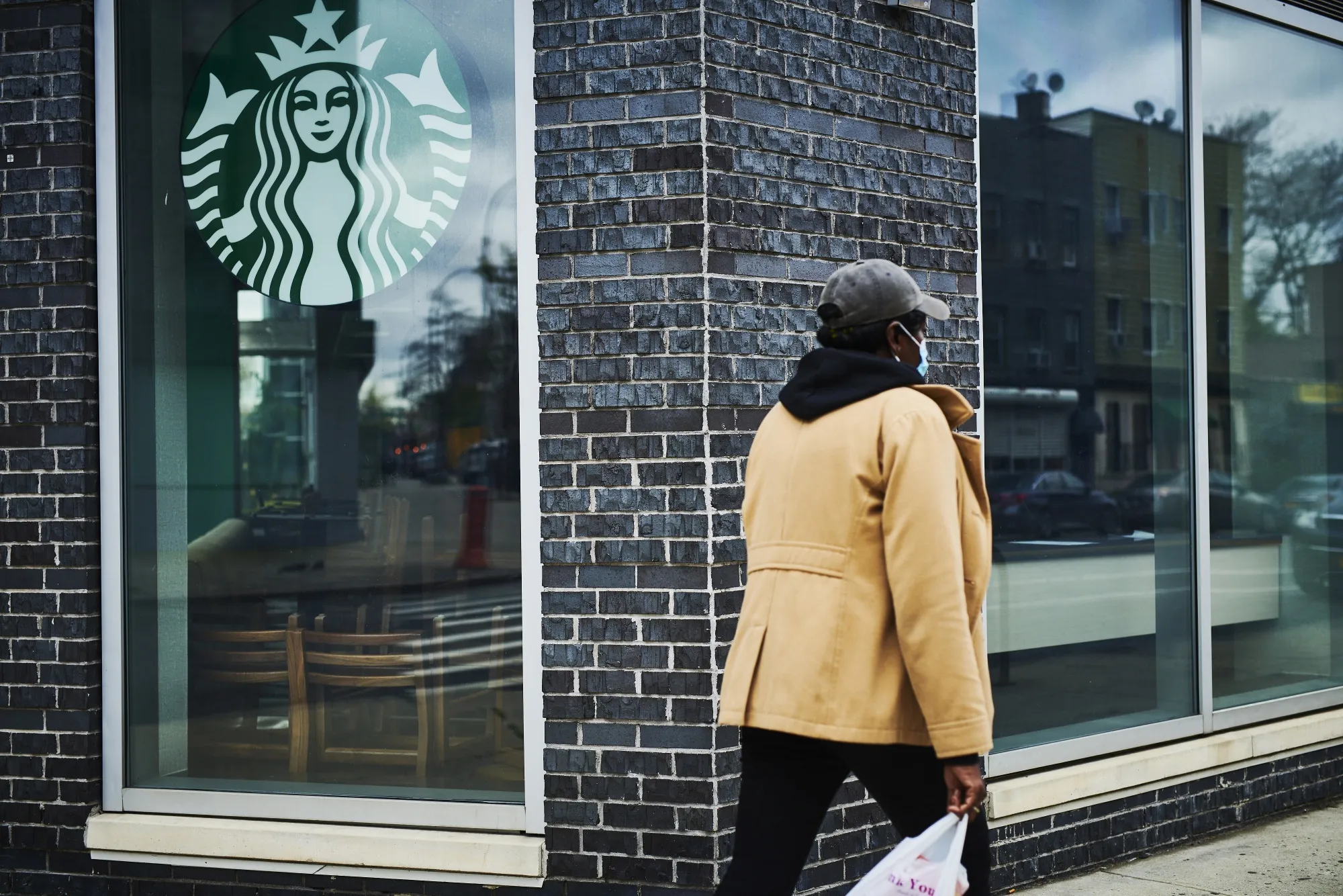A pedestrian wearing a protective mask walks past a temporarily closed Starbucks location.