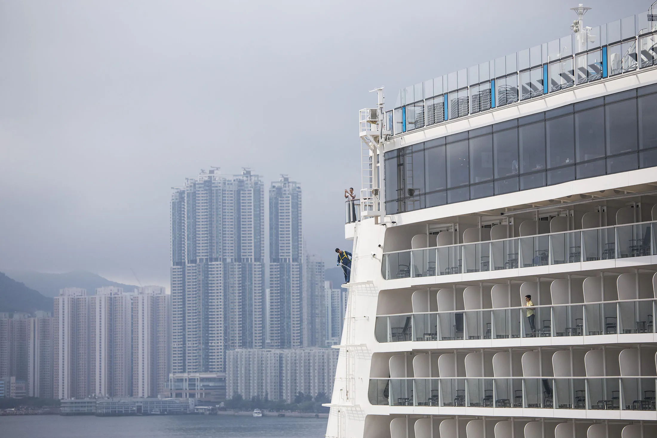 A passenger looks out from the balcony of a room onboard the Royal Caribbean Cruises Ltd. Ovation of the Seas Quantum-class cruise ship docked at the Kai Tak Cruise Terminal as residential buildings stand in the background in Hong Kong, China, on Friday, April 21, 2017.
