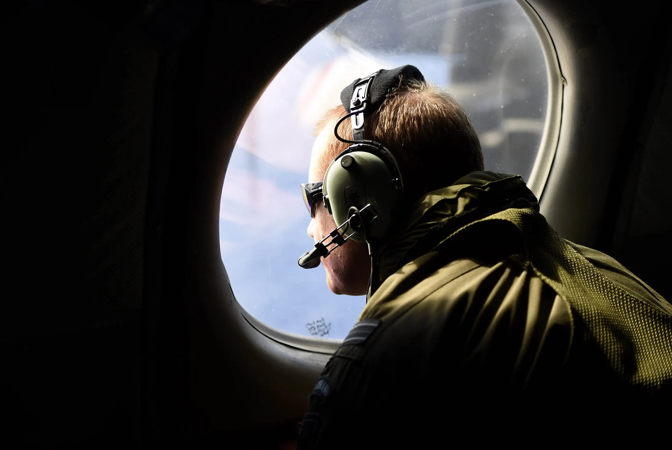A crew member looks out an observation window aboard a Royal New Zealand Air Force maritime search aircraft.

