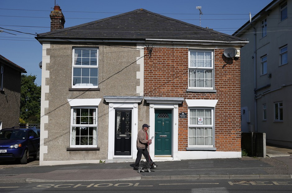 A man walks a dog past semi-detached homes in Brightlingsea, southeast England, May 16, 2014. 