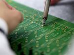 An employee solders components onto a circuit board.