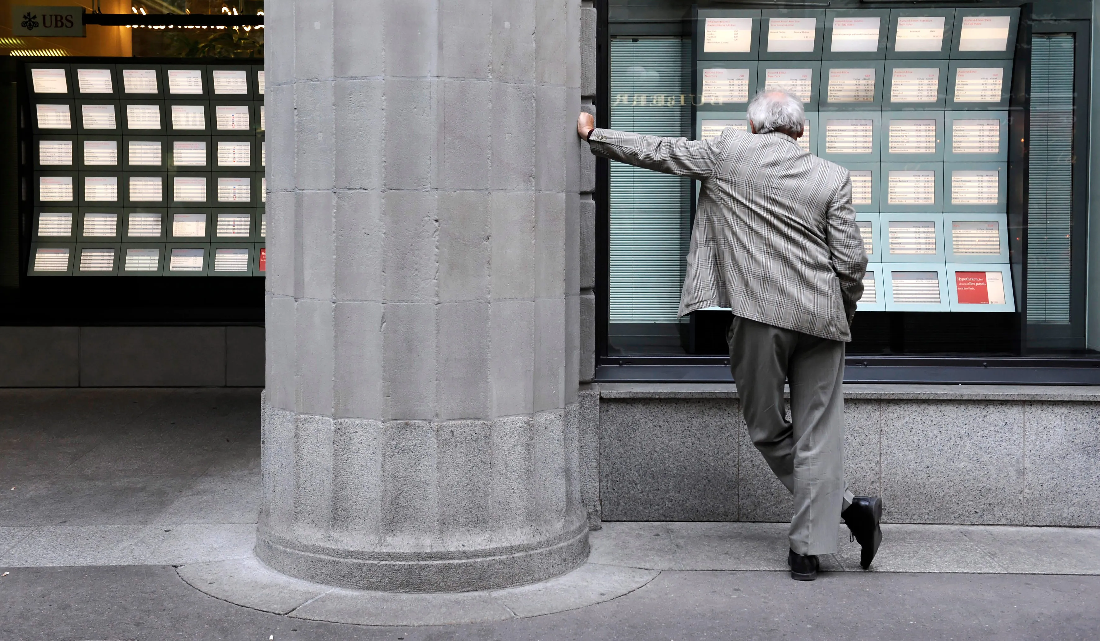 A pedestrian looks at stock tickers in a window at the UBS A