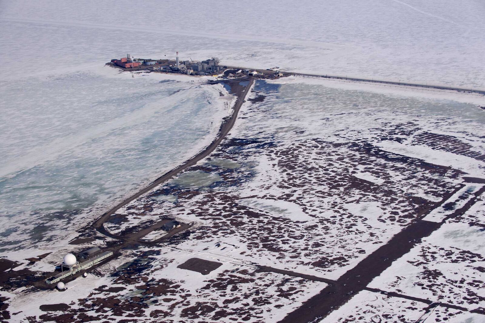 A ConocoPhillips seawater treatment plant and adjacent Eni facility on a spit of land on Alaska’s north coast, surrounded on three sides by the frozen Beaufort Sea. Nearby along the coast sits a NORAD military radar station.