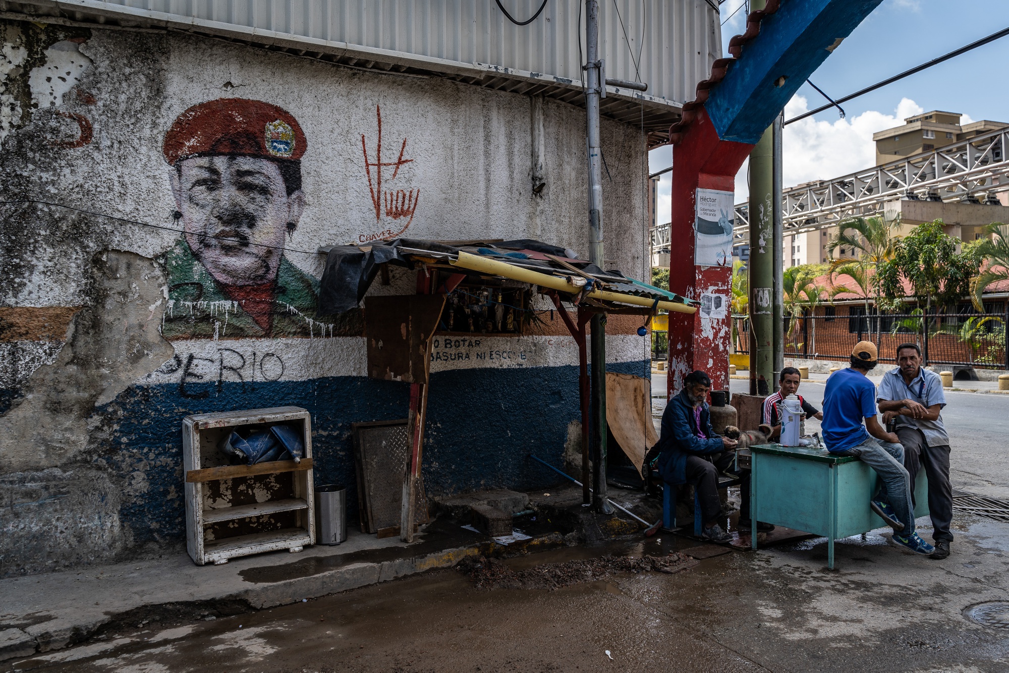 People sit next to a mural of the late Hugo Chavez in the Petare neighborhood of Caracas.