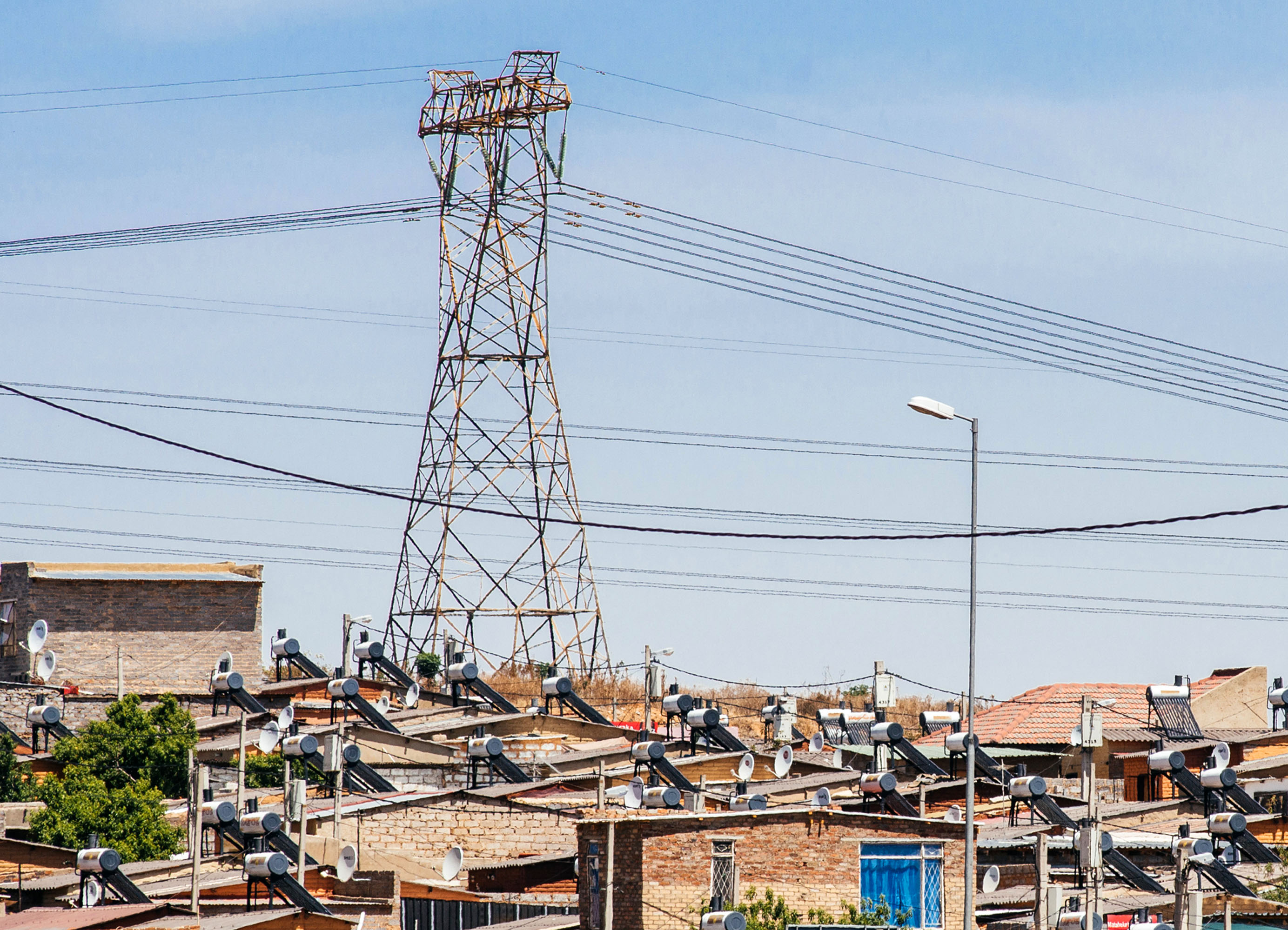 A pylon tower carries electrical power lines over residential shacks, some equipped with solar power geysers on their roofs, in the Alexandra township outside Johannesburg, South Africa.