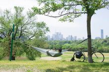 A man sits in a hammock facing the Toronto city skyline in Riverdale Park East, located along the Beltline Trail.