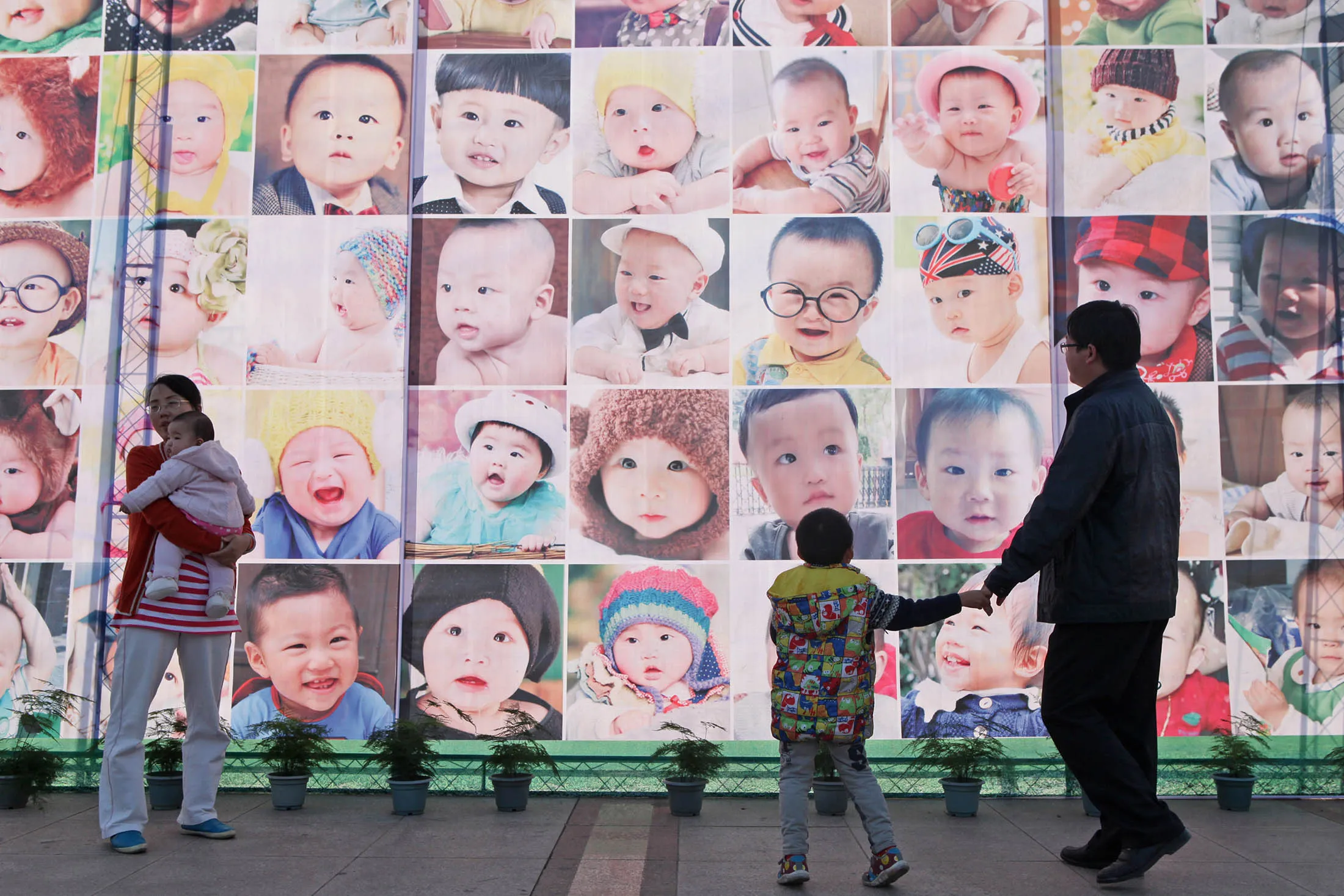 People pass a poster printed with babies' faces in Taizhou, Zhejiang Province of China.
