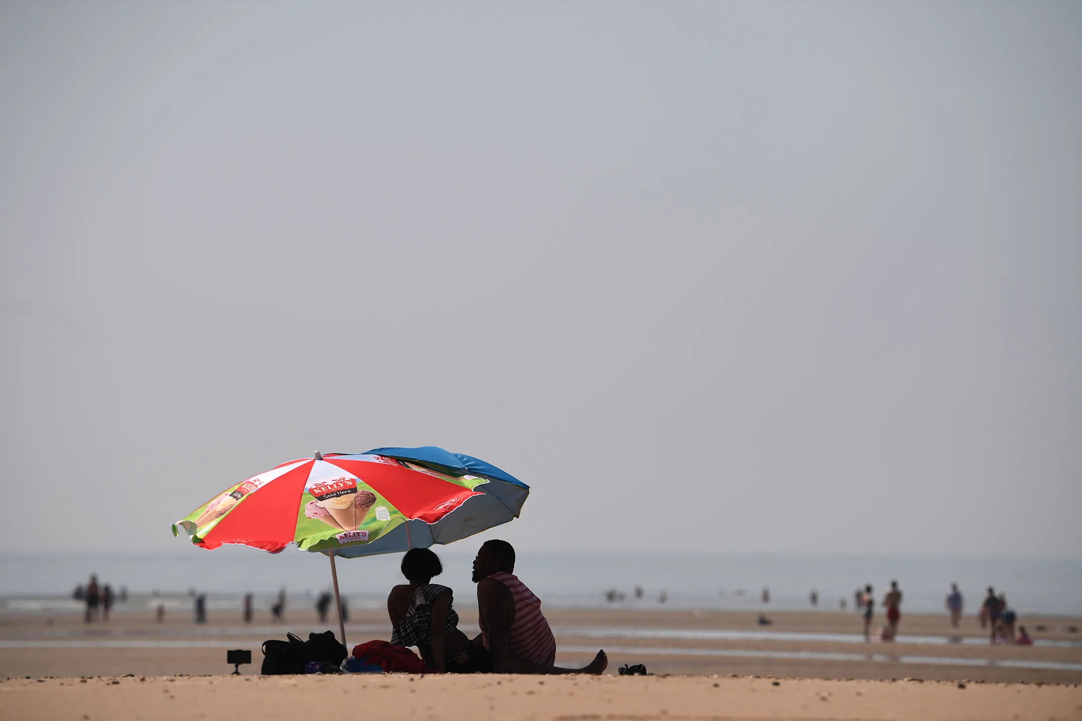 Beach-goers shelter under an umbrella in Camber Sands, England, on July 25.