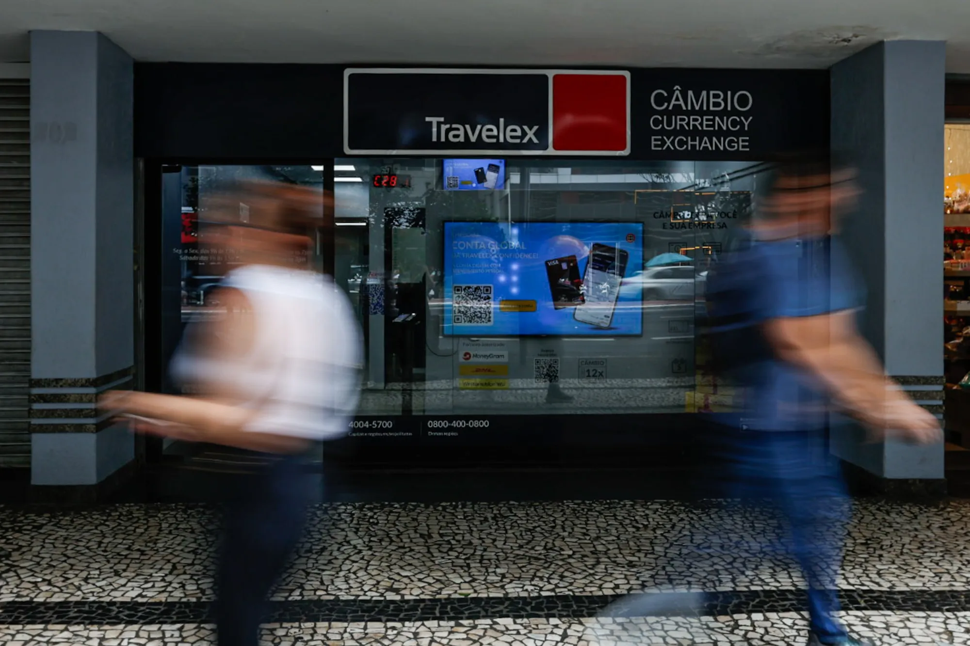 Pedestrians walk past a currency exchange shop on Paulista Avenue in Sao Paulo, Brazil.