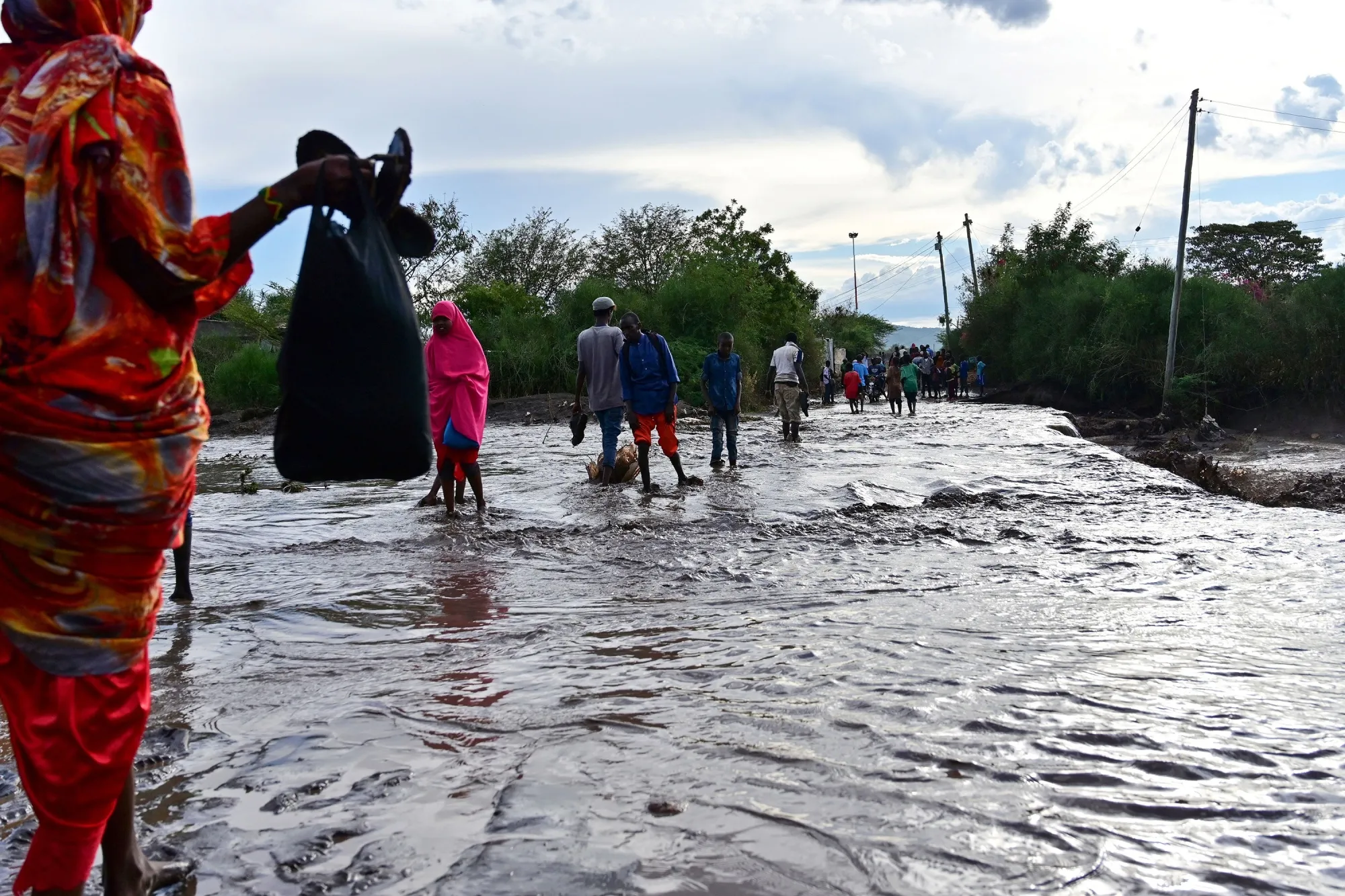 People wade across a submerged road following flash flooding in the semi-arid northern town of Isiolo, Kenya