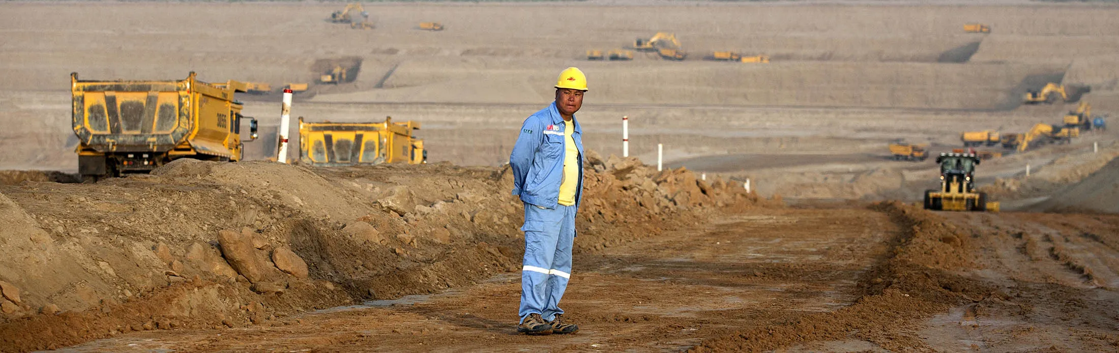 A Chinese foreign worker stands on the floor of an open pit mine as excavators and dumper trucks used to transport excavated silica sand operate in the background at Sindh Engro Coal Mining Co.'s site in the Thar desert, Pakistan, on Wednesday, March 8, 2017.
