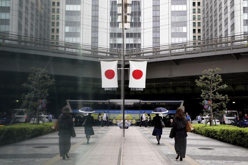 Pedestrians walk past the Japanese national flag reflected in a window of a department store  in Tokyo. Photographer: Kiyoshi Ota/Bloomberg