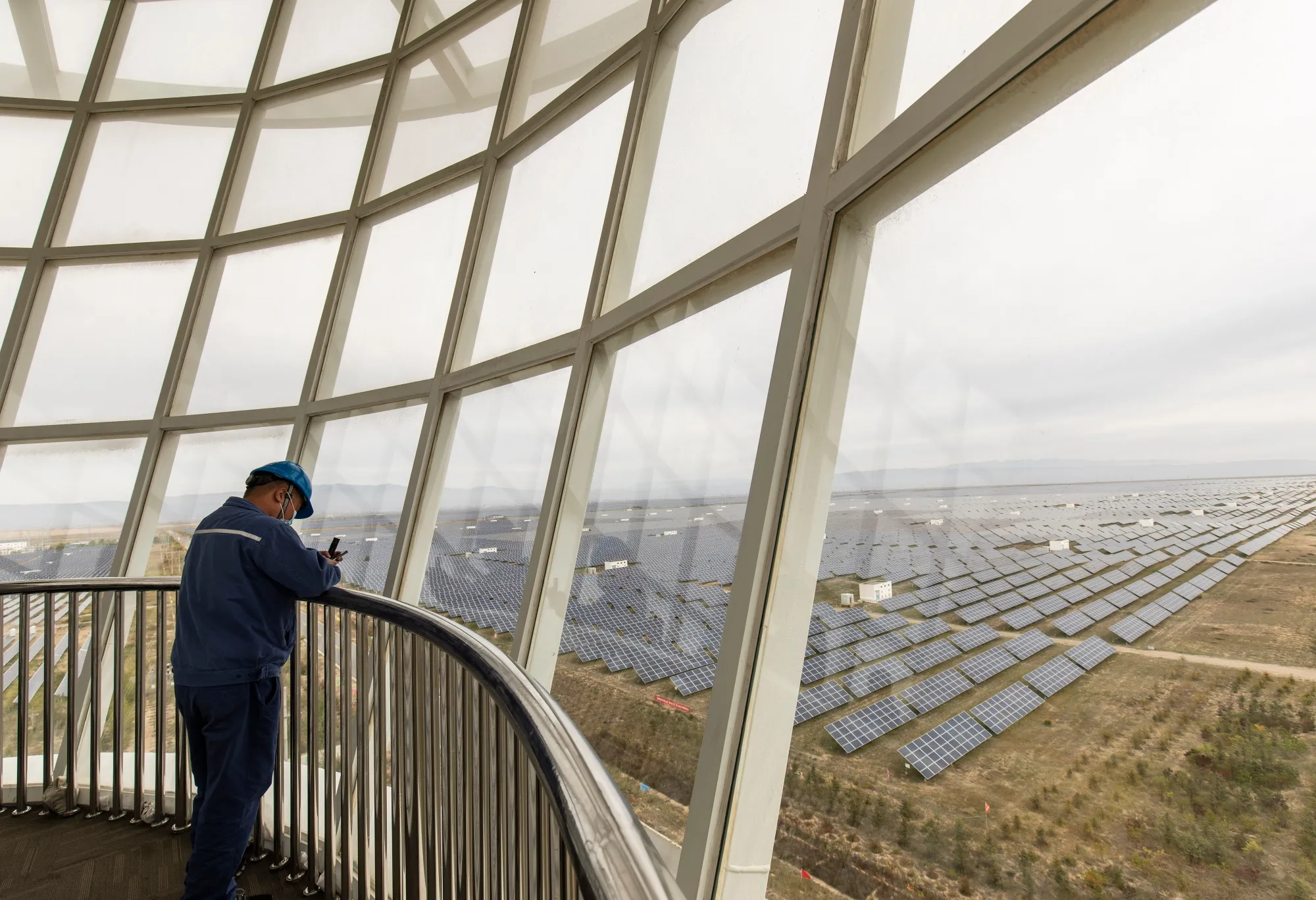 A worker stands in an observation tower over looking photovoltaic panels at a solar farm in Gonghe County, Qinghai province, China.