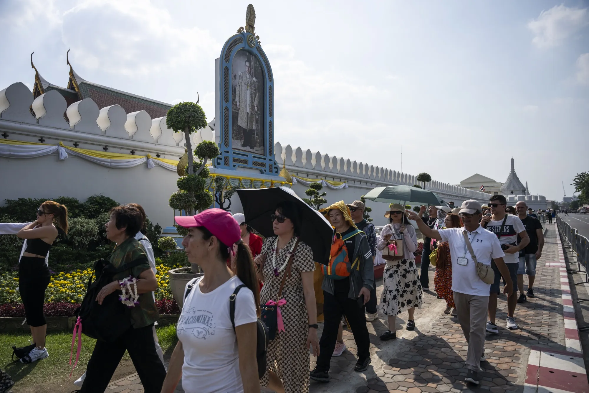 Tourists walk along the wall of the Grand Palace in Bangkok.
