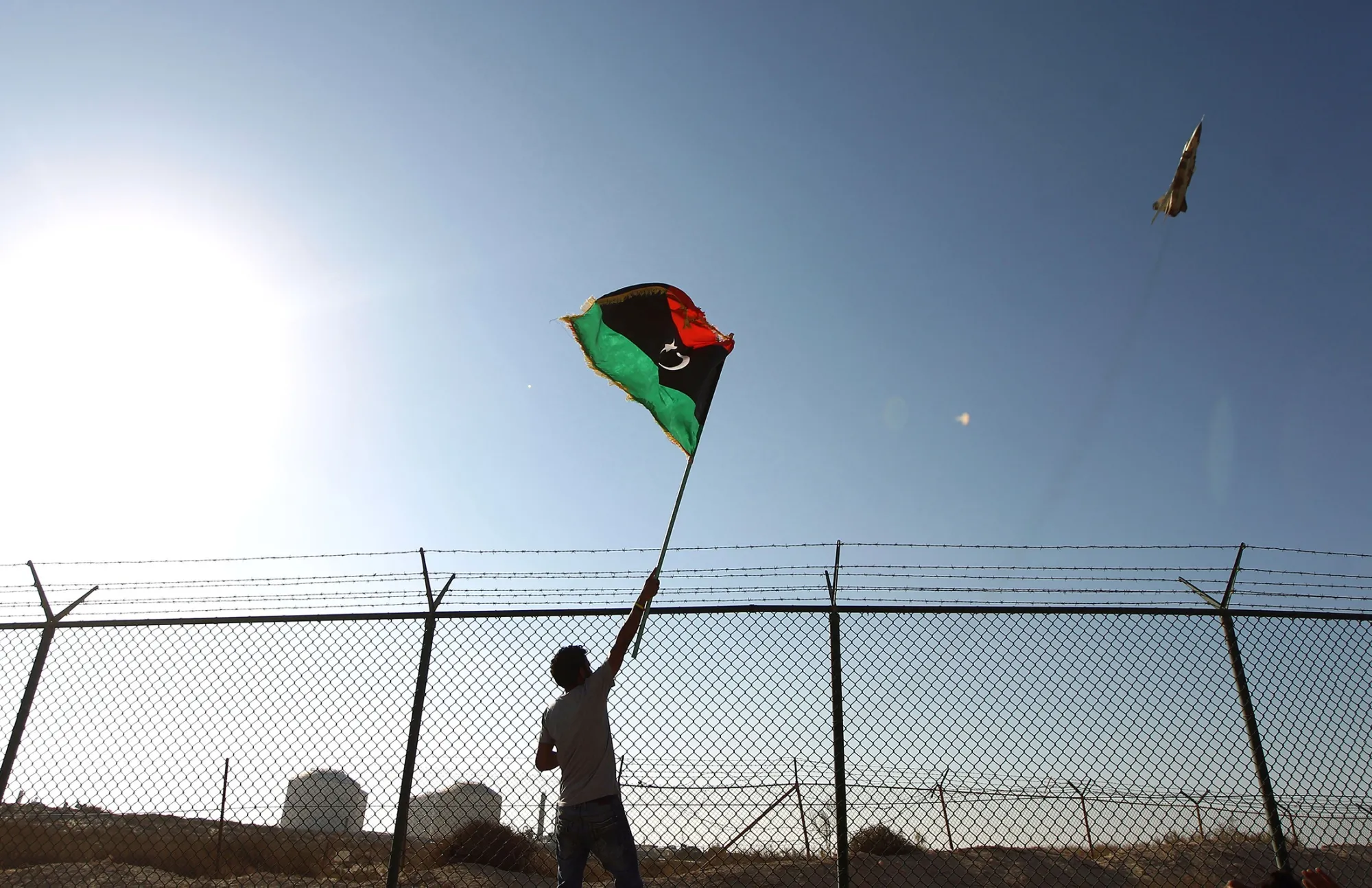 A man waves a Libyan flag as fighter jet flies past.